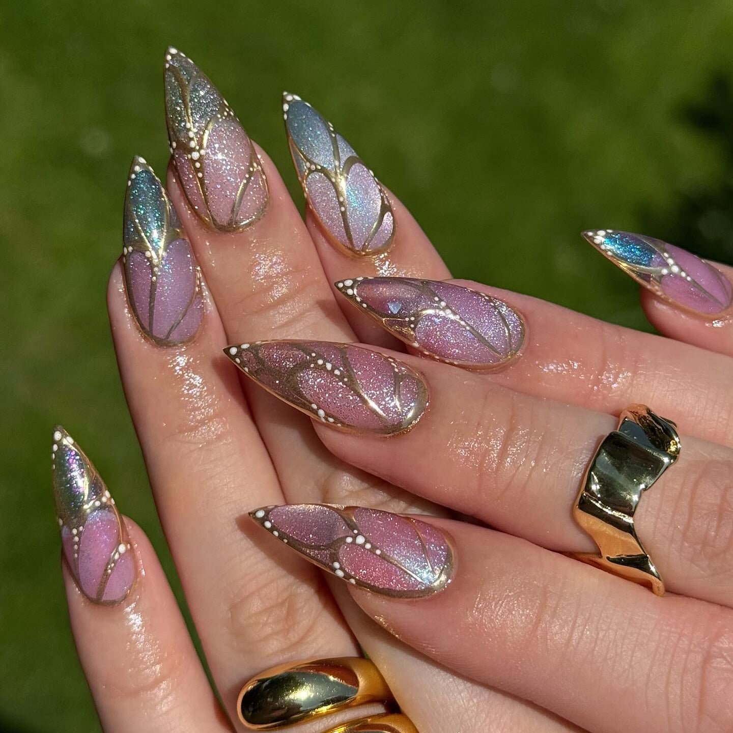 Nails with butterfly design and gold accents against a green bacground